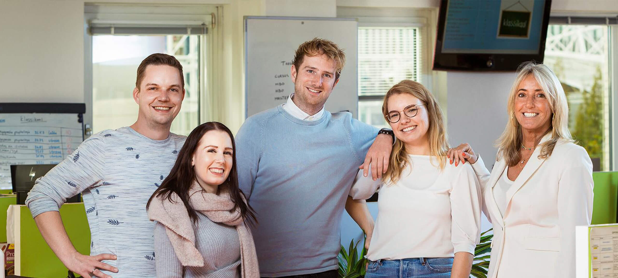 Een groep collega's staan glimlachend naast elkaar op kantoor bij NTI